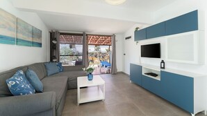 Ein modernes Wohnzimmer mit einer Couch, einem Couchtisch, einem Fernseher und Blick durch eine Glastür.