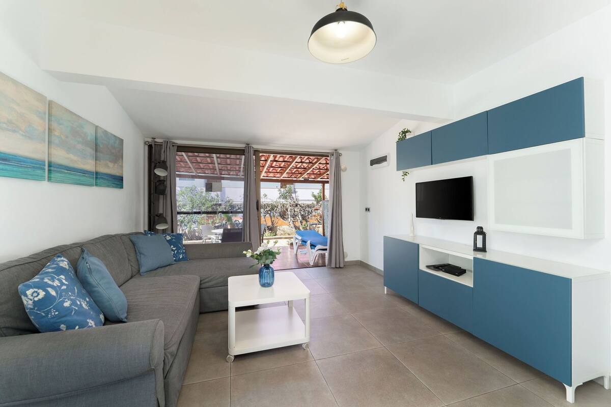 A modern living room with a sofa, coffee table, TV, and a view through a glass door.