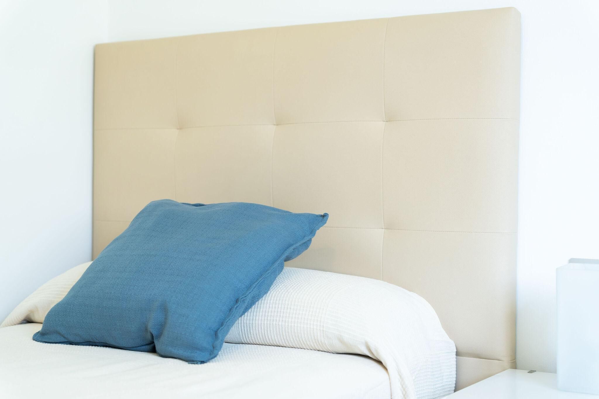 A bed with a beige headboard, a blue pillow, and a white pillow.