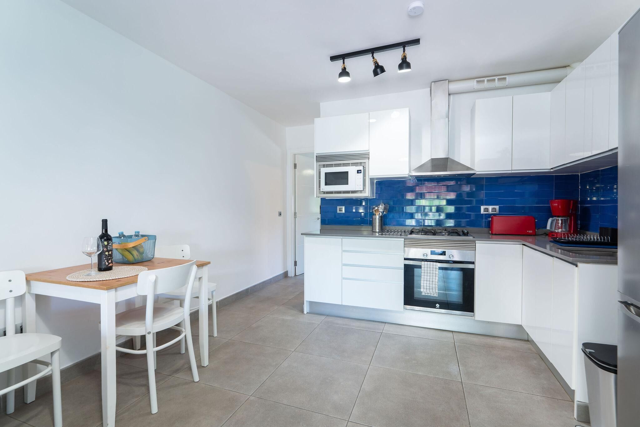 A modern kitchen with white cabinets, a microwave, a stove, and a red coffee maker.