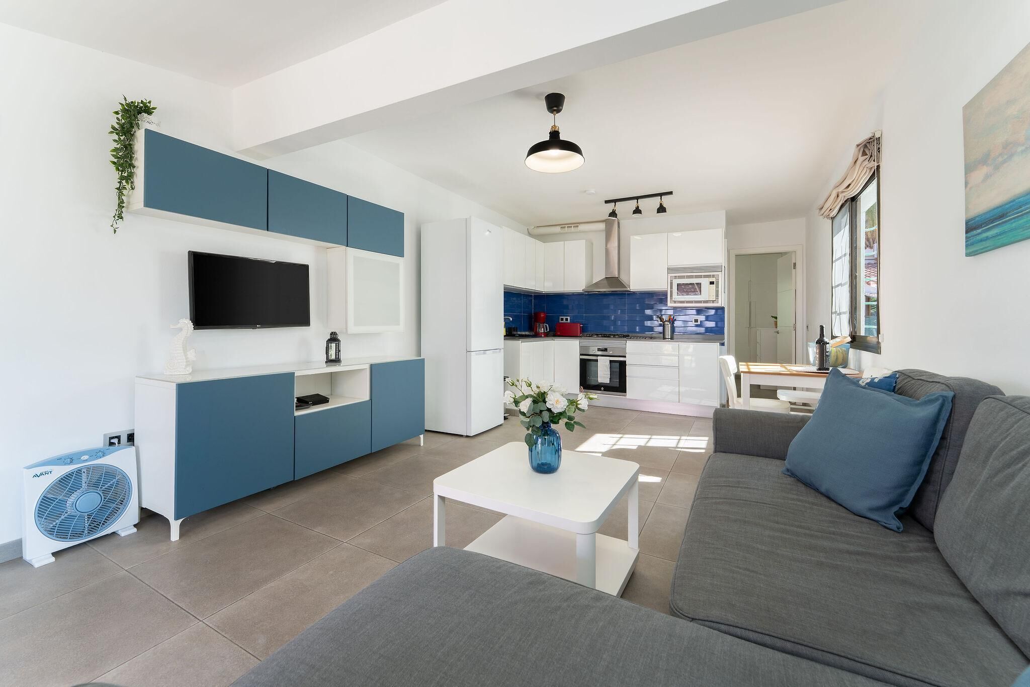 Una sala de estar moderna con un sofá gris, una mesita de centro blanca y un jarrón azul.