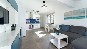 Eine moderne Küche mit weißen Schränken, eine Essecke mit einem weißen Tisch und Stühlen, und ein graues Sofa mit einem Blumenarrangement.