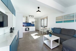A modern kitchen with white cabinets, a dining area with a white table and chairs, and a gray sofa with a vase of flowers.