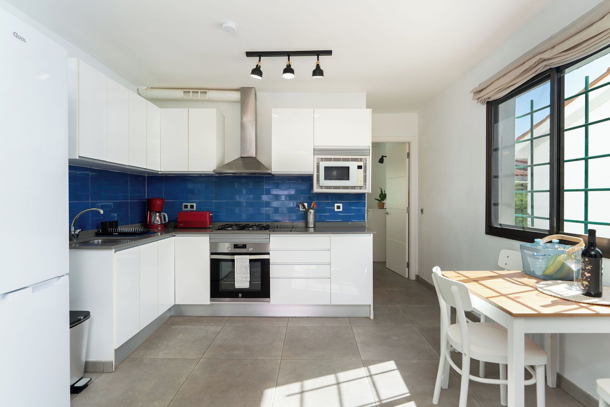 Et moderne køkken med hvide skabe, blå backsplash, gasblus, mikroovn og et vindue med udsigt.