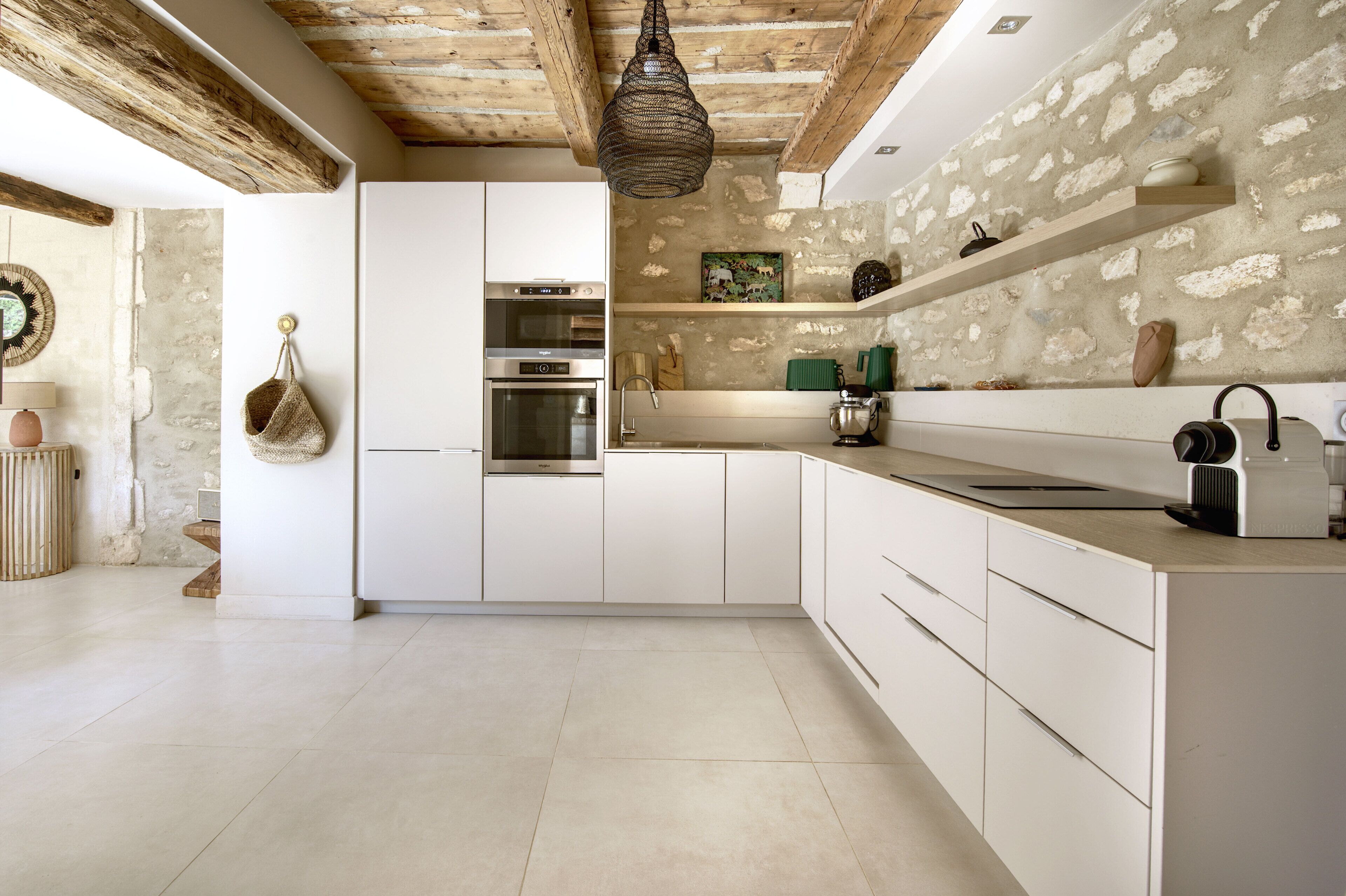 Une cuisine moderne avec des meubles blancs, un four encastré et un mur en pierre.