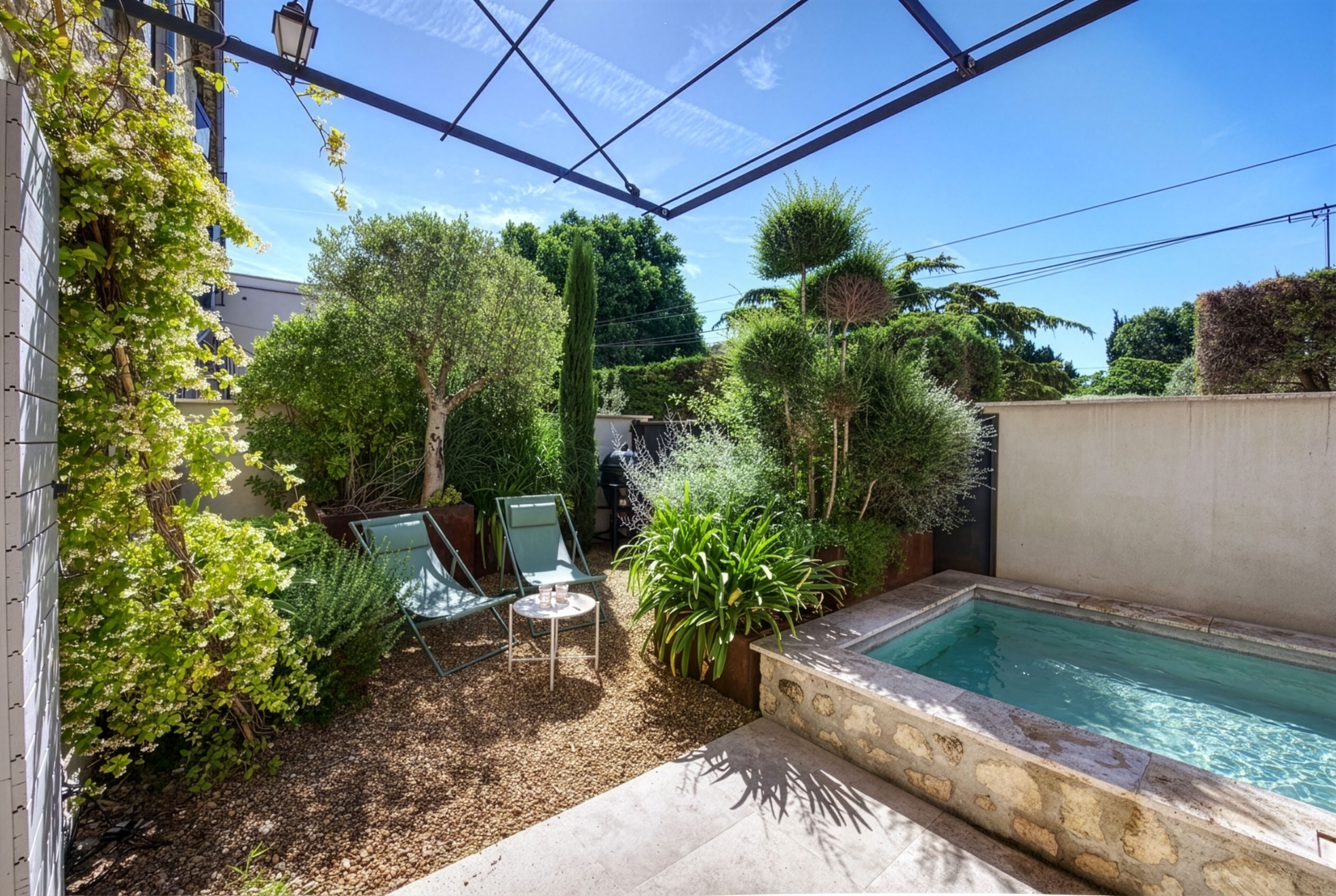 Un patio privé avec une piscine, entouré de différentes plantes et agrémenté d’une pergola.