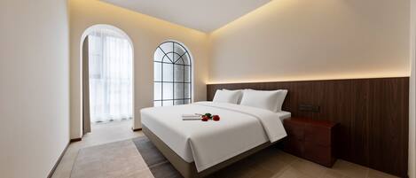 A modern hotel room with a large bed, a nightstand, a wooden headboard, a large window with a view, and a small rug.