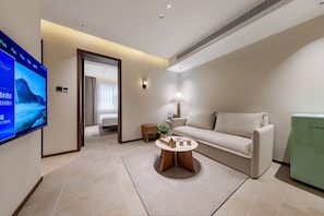 A modern hotel room with a large flat-screen TV, a sofa, a coffee table, and a small side table with a lamp. - APOLLO COURTYARD HOTEL (Zhangjiajie)
