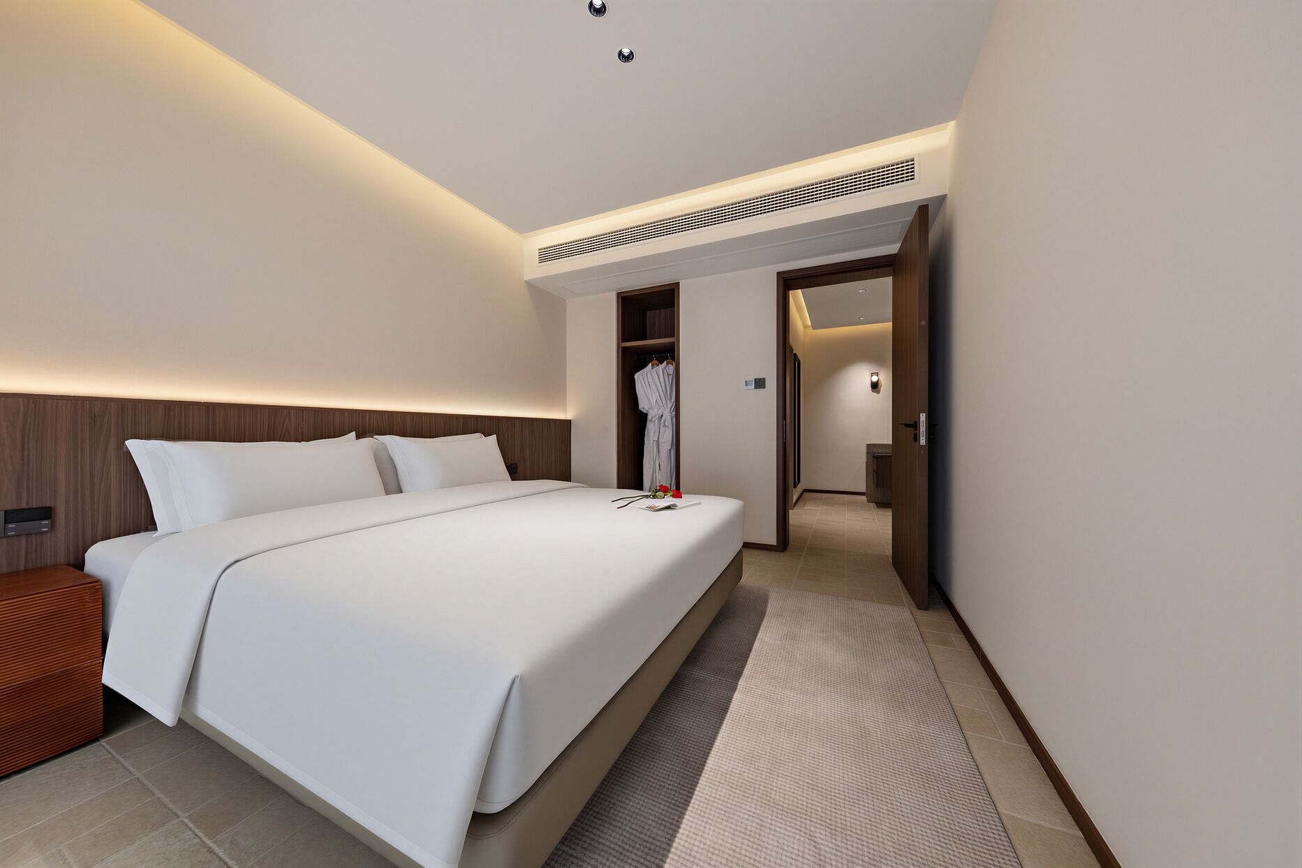 Una habitación de hotel moderna con una cama grande, un vestidor y un baño visible a través de una puerta abierta.