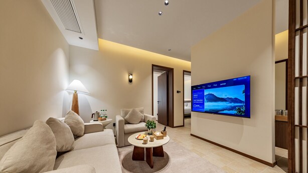 A modern living room with a sofa, armchairs, a coffee table, and a flat-screen TV mounted on the wall. - APOLLO COURTYARD HOTEL (Zhangjiajie)