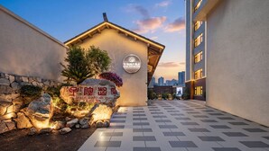 A hotel entrance with a stone wall, a signboard, and a paved walkway leading to a building. - APOLLO COURTYARD HOTEL (Zhangjiajie)