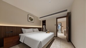 A modern hotel room with a large bed, a wooden headboard, a bedside table, a robe hanging on a rack, and a tray with a bottle and glasses. - APOLLO COURTYARD HOTEL (Zhangjiajie)