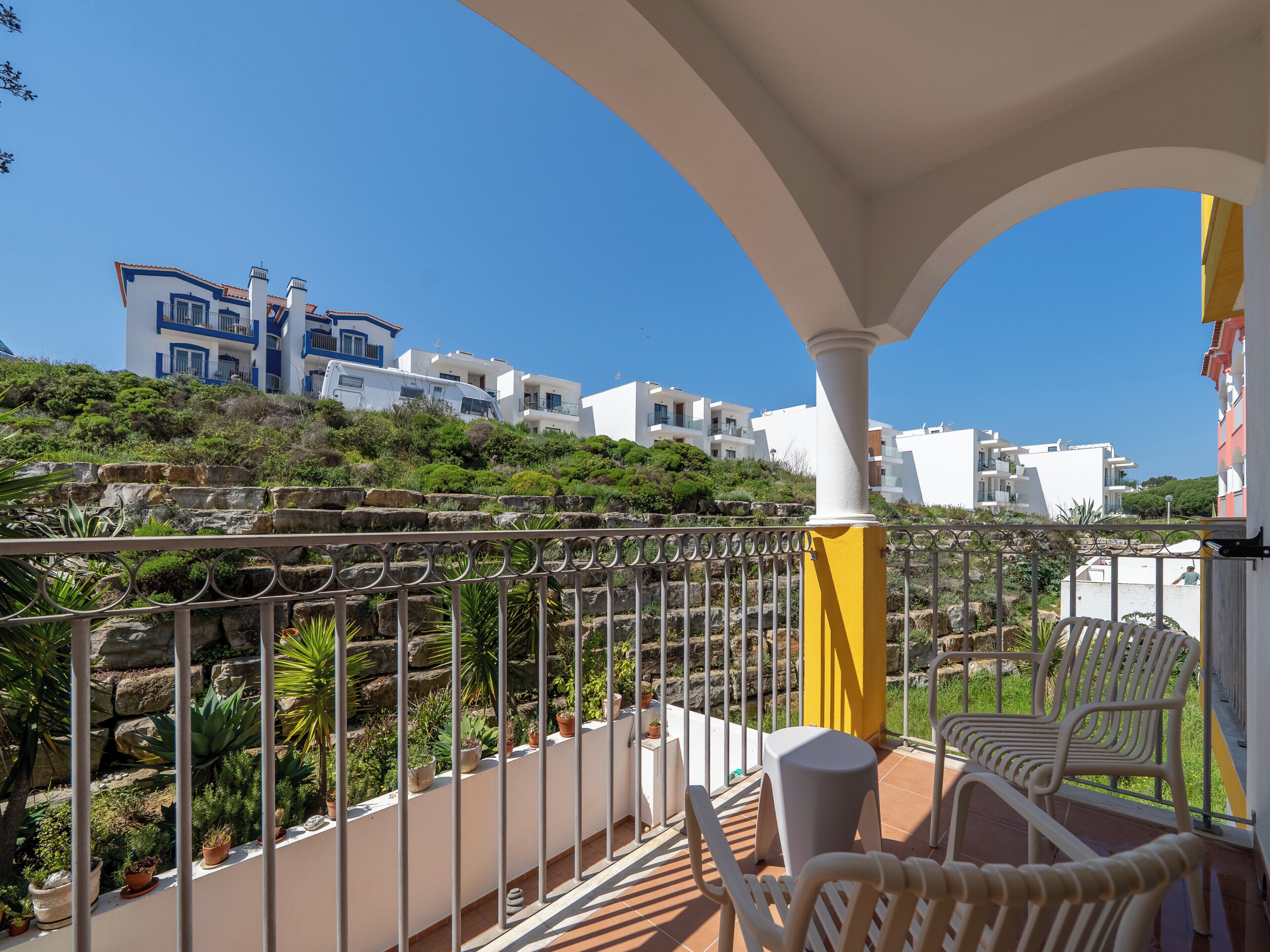 A balcony with white chairs, a small table, and potted plants.