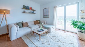 Uma sala de estar com sofá, mesa de centro, abajur e uma janela grande com vista.