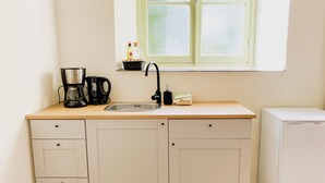 A compact kitchen with a sink, a coffee maker, a bottle, and a small refrigerator. - Modern Studio 1 in Historic Abbey (Cadier en Keer)