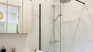 A modern bathroom with a glass-enclosed shower, a white sink, and a mirror above the sink. - Modern Studio 1 in Historic Abbey (Cadier en Keer)