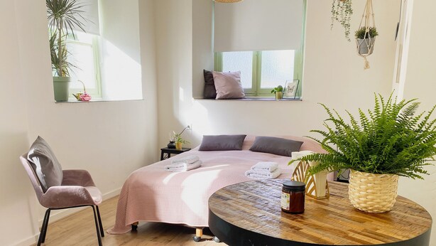 A cozy bedroom with a bed, bedside tables, a chair, a round table, and potted plants. - Modern Studio 1 in Historic Abbey (Cadier en Keer)