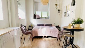 A bedroom with a bed, bedside tables, a chair, a small table, a hanging light, and a window. - Modern Studio 1 in Historic Abbey (Cadier en Keer)