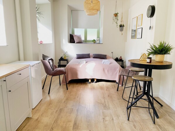 Quarto com cama, mesas de cabeceira, uma cadeira, uma mesinha, luminária pendente e janela.