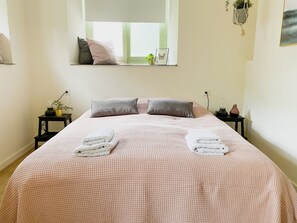 Cama bem arrumada com colcha quadriculada rosa e branca, dois travesseiros e duas toalhas dobradas.