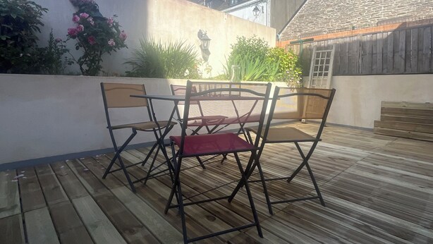 A patio with a table and chairs, surrounded by a low wall with plants and a stone building in the background. - 4 P. house in a charming Breton village (Pont-Aven)