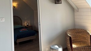 A room with a sloped ceiling, a bed with a blue bedspread, a wicker chair, a small stool, and a hanging lantern. - 4 P. house in a charming Breton village (Pont-Aven)