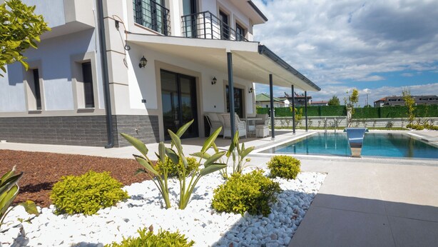 A modern house with a pool, white gravel landscaping, and a covered patio area.