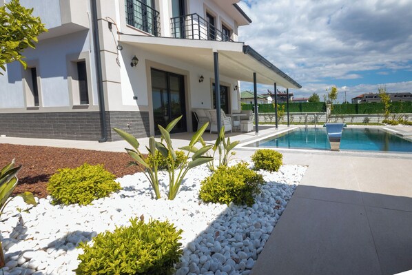 A modern house with a pool, white gravel landscaping, and a covered patio area.