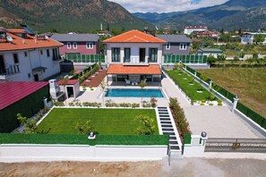 A residential property with a swimming pool, a well-maintained lawn, and a view of the surrounding mountains.