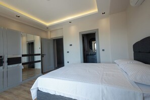 A modern bedroom with a large bed, a wardrobe, a mirror, and a doorway leading to another room.
