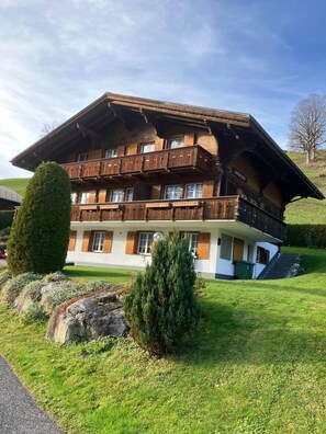 A multi-story wooden chalet with balconies, a stone staircase, and a well-maintained lawn. - Chalet Amaryllis – Eiger View Apartment (Grindelwald)