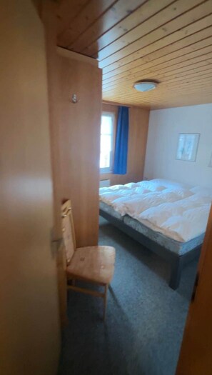 Une pièce avec un lit, une chaise, une fenêtre avec des rideaux bleus et un plafond en bois.