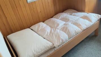 Une petite pièce en bois, avec un lit simple, un tableau encadré au mur et une petite table de chevet en bois sur laquelle se trouve une lampe.