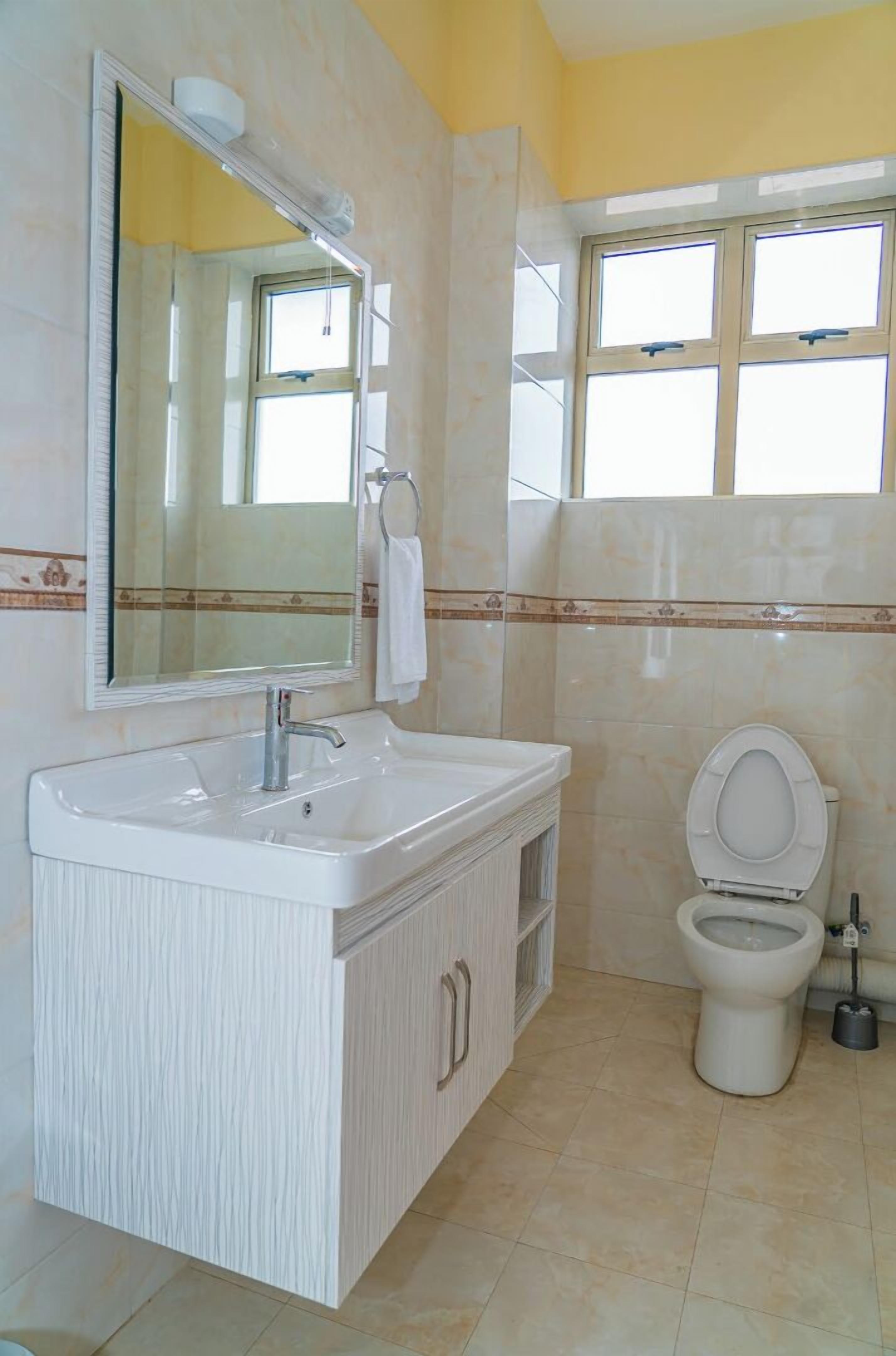 Un baño con tocador blanco, un espejo grande, un inodoro y una ventana.