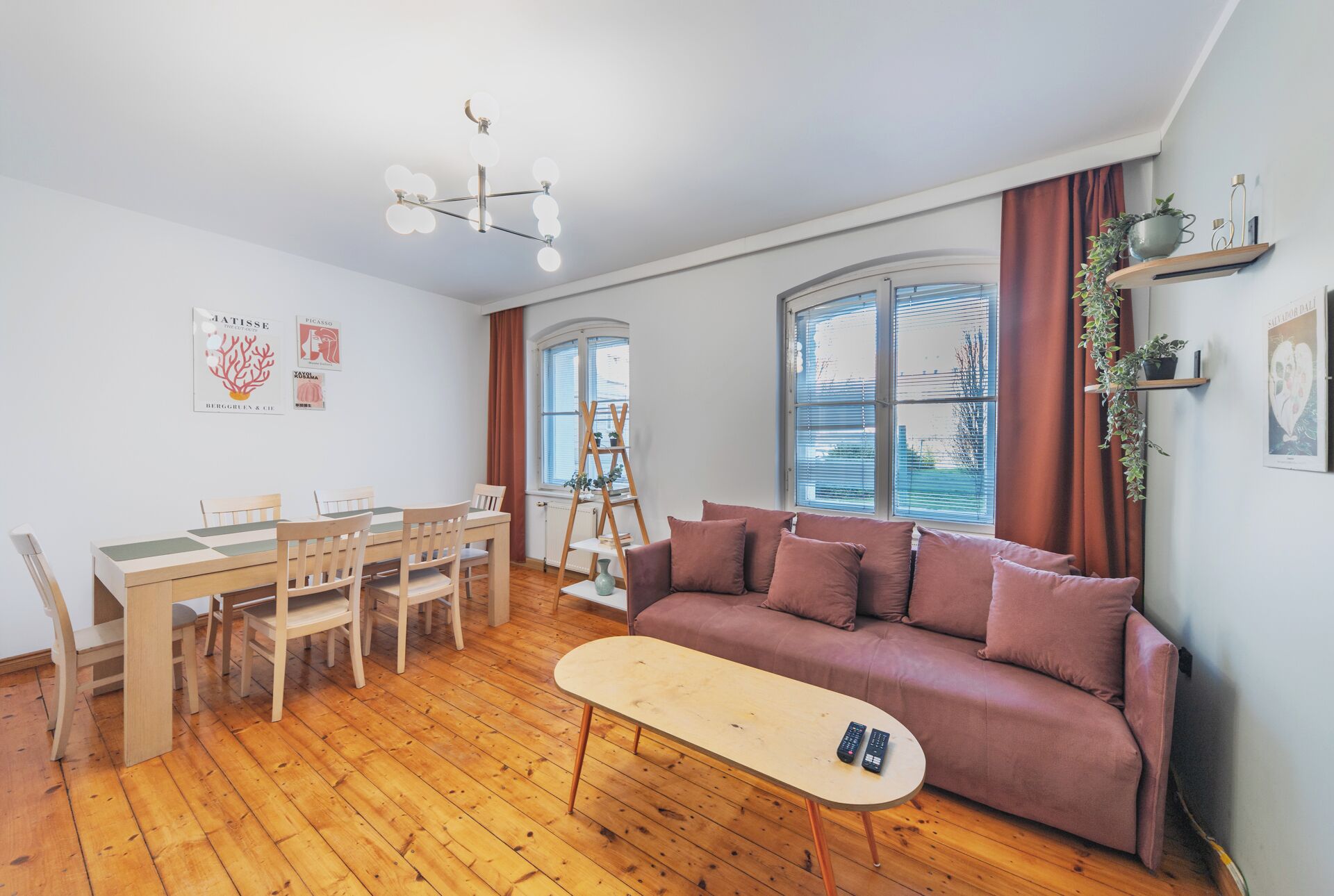 A living room with a wooden floor, a sofa, a table, and a dining set.