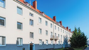 Una hilera de casas urbanas con ventanas y techos rojos similares, un pequeño espacio cubierto de césped y un árbol a la derecha.