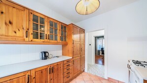 Una cocina con armarios de madera, encimera blanca, estufa y una lámpara colgante.