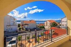 A balcony with a view of a coastal town, a stone wall, and a parked car. - Studio in Crikvenica with pool, sea view & parking space (Crikvenica)