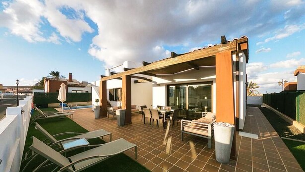 Un patio techado al aire libre con zona de comedor, piscina y césped.