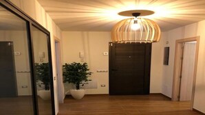 Un pasillo con piso de madera, una planta grande en maceta, una lámpara colgante moderna y una puerta oscura.