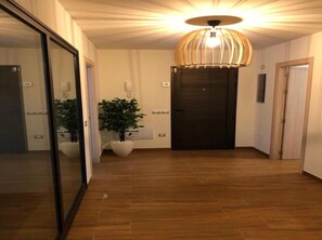 Ein Flur mit Holzboden, einer großen Topfpflanze, einer modernen Pendelleuchte und einer dunklen Tür.