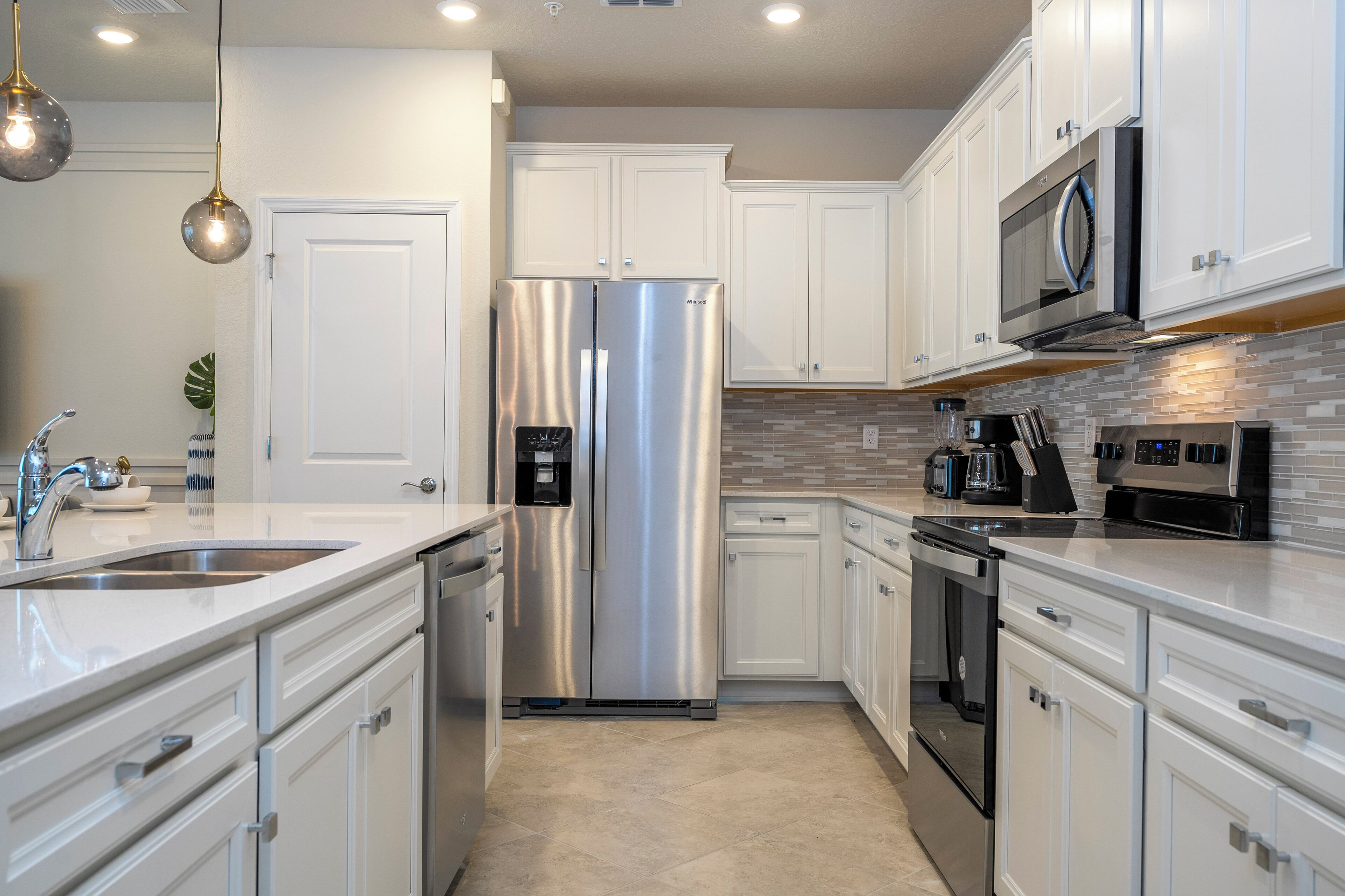 A modern kitchen with white cabinets, stainless steel appliances, and a tiled backsplash.