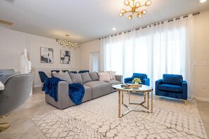 A modern living room with a sofa, two armchairs, a coffee table, and a chandelier. - New Home w/ Exclusive Décor, Private Pool, BBQ & Windsor Cay Resort Access! (Clermont)