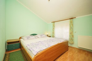 Une chambre à coucher avec un lit en bois, une table de chevet, une commode verte, un radiateur et une fenêtre avec des rideaux.