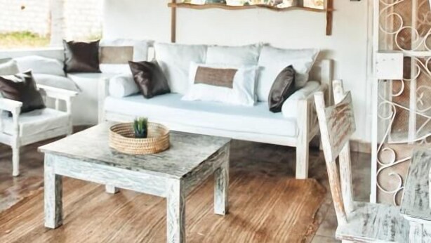 Ein rustikales Interieur mit einem Strohdach, einem weißen Sofa, einem Holztisch und einer dekorativen Deckenleuchte.