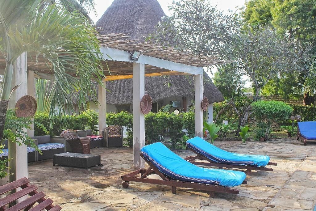 A covered outdoor seating area with lounge chairs and a thatched-roof structure.
