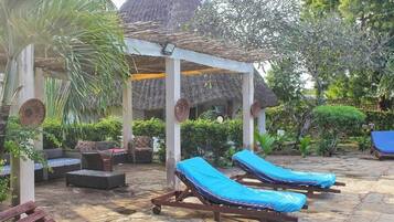 A covered outdoor seating area with lounge chairs and a thatched-roof structure.
