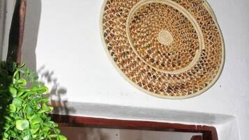 A room with a woven mat on the wall, a wooden door, and a potted plant.