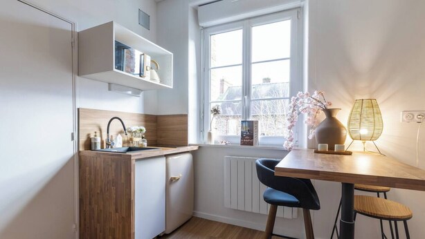 Une cuisine compacte dotée d’un four encastré, d’une fenêtre offrant une belle vue et d’un coin repas simple avec une table et des chaises.