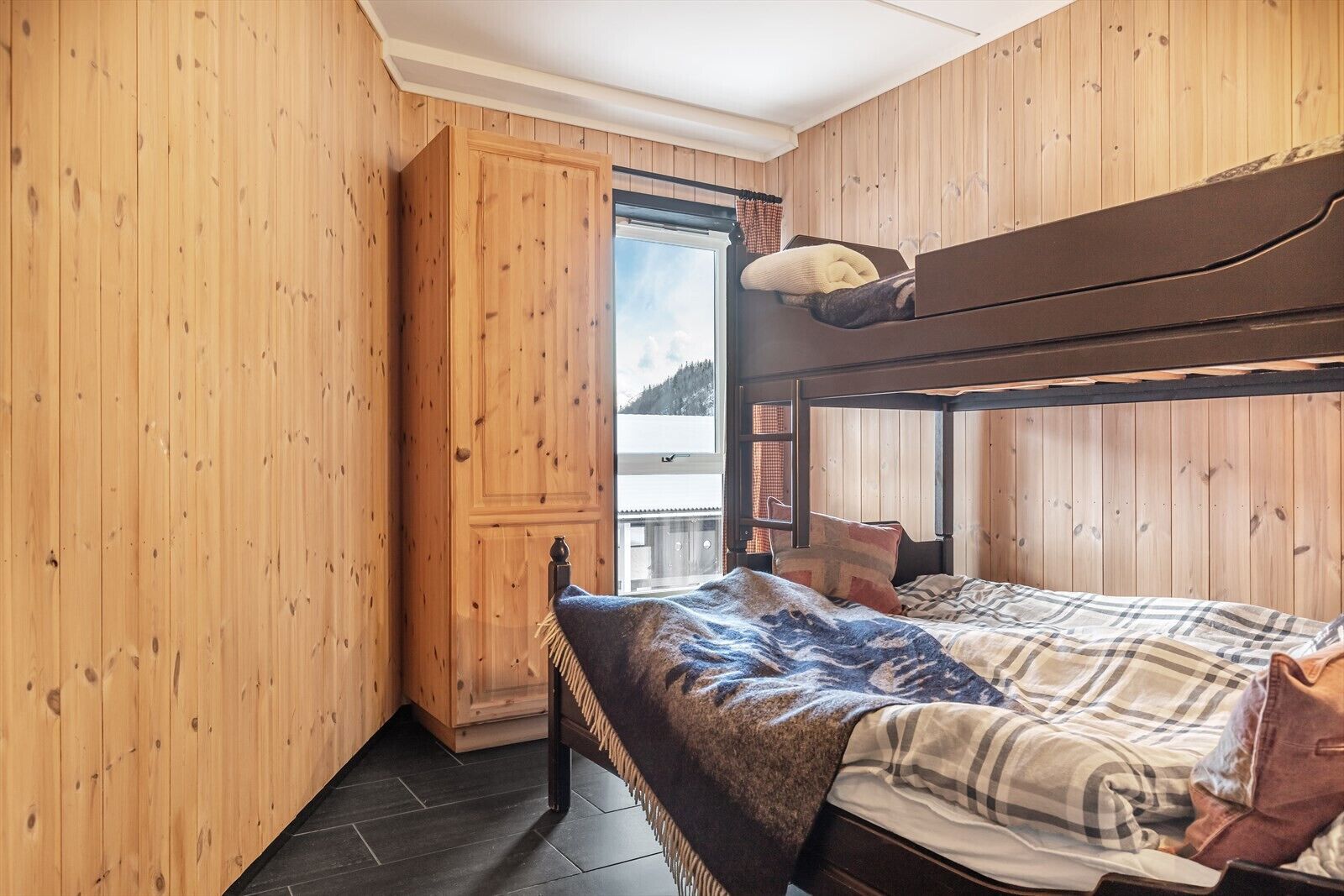 A wooden cabin room with a bunk bed, a window with a view, and a door.